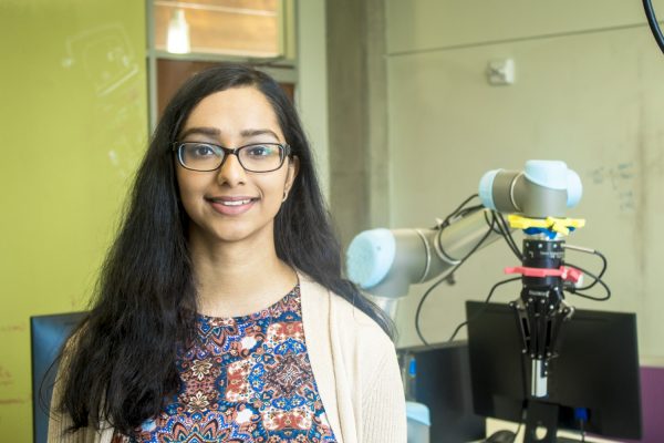 Gopkika Ajaykumar stands in front of a robot end effector.