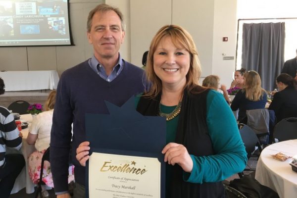 Tracy Marshall and Greg Hager pose together for a picture. Marshall holds a certificate that reads "Excellence Certificate of Appreciation, Tracy Marshall."