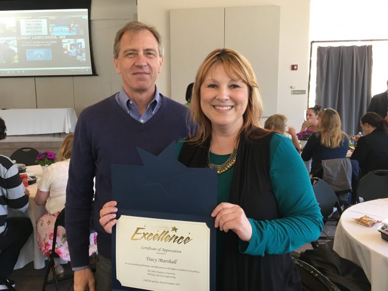 Tracy Marshall and Greg Hager pose together for a picture. Marshall holds a certificate that reads "Excellence Certificate of Appreciation, Tracy Marshall."