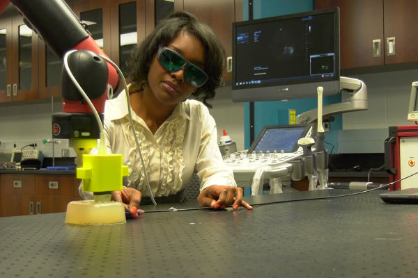 Wearing safety goggles, Muyinatu Bell works in her lab with a robot end effector.