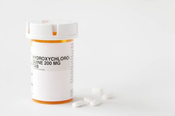 A pill bottle and white pills. The bottle is titled Hydroxychloroquine 200 MG tab.