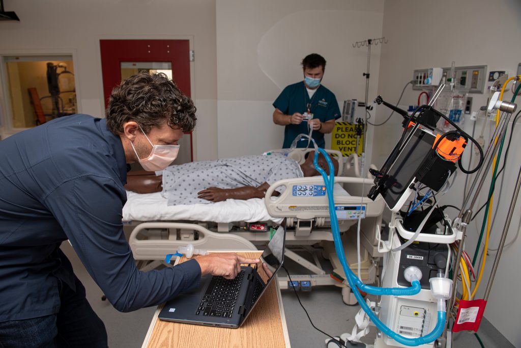 Jonathan Cope and Mechanical Engineering Professor Axel Krieger work in the Johns Hopkins Hospital Bio-Containment Unit to test a robot that adjusts ventilator settings while being controlled via a tablet from outside the patient's room in order to avoid unnecessary patient contact.