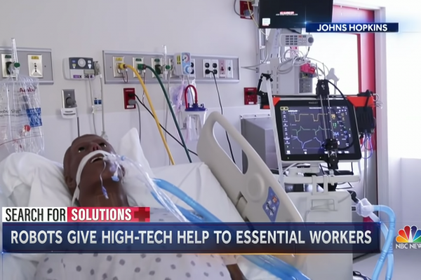 A screencap of news coverage titled "Search for Solutions: Robots give high-tech help to essential workers, Johns Hopkins." A mannequin is set up in a hospital bed.
