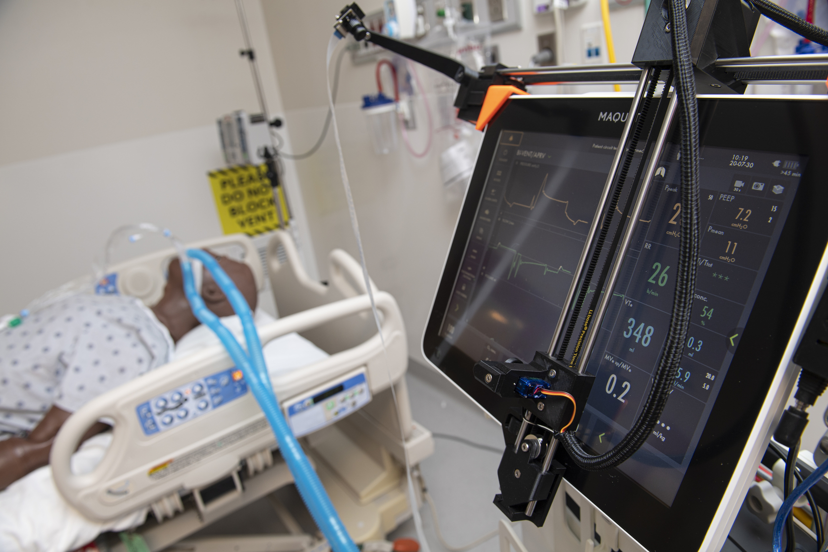 A monitor showing vital signs. It is connected to a mannequin in a hospital bed.