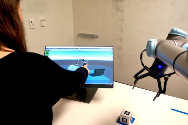 A student points on a screen while a robot arm hovers nearby.