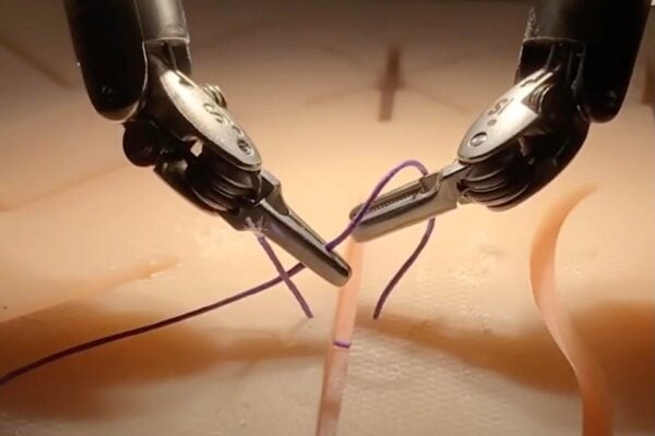 Two surgical robot arms hold and tie suture material in a simulated surgical setting.