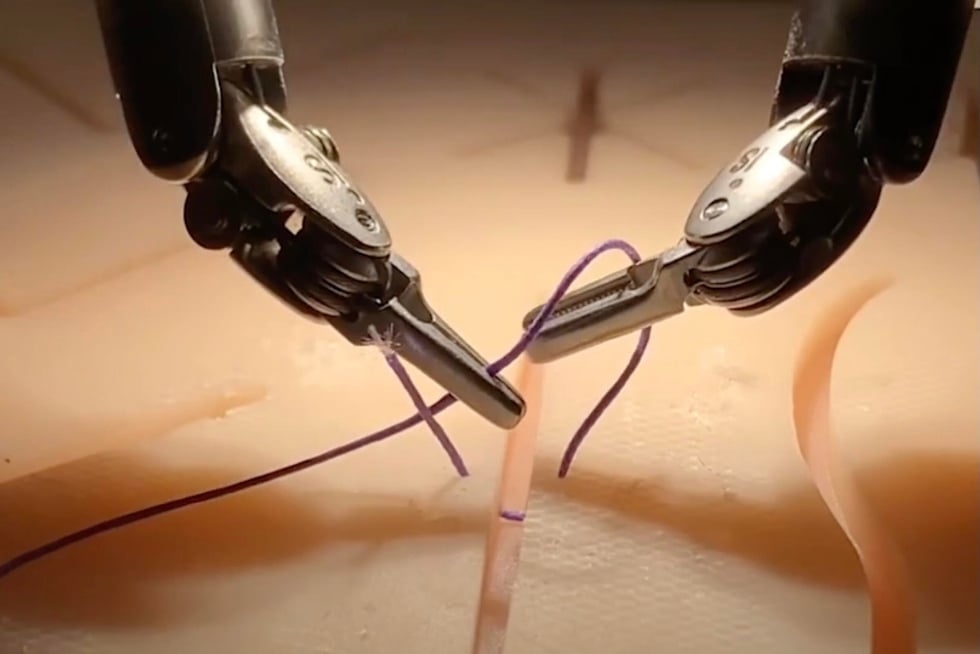 Two surgical robot arms hold and tie suture material in a simulated surgical setting.