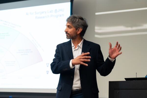 Swaroop Vedula gestures in front of a projector screen.