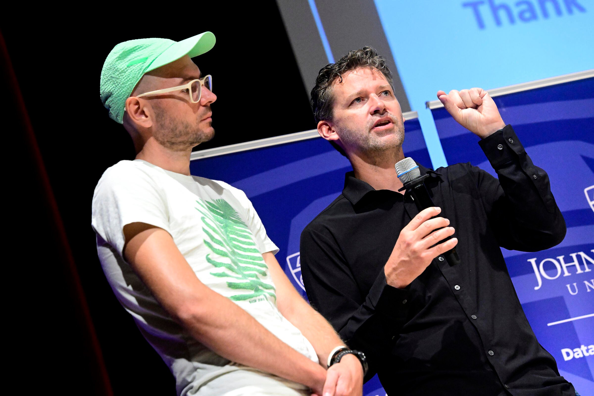 Mathias Unberath and Axel Krieger on a stage. Krieger holds a microphone.