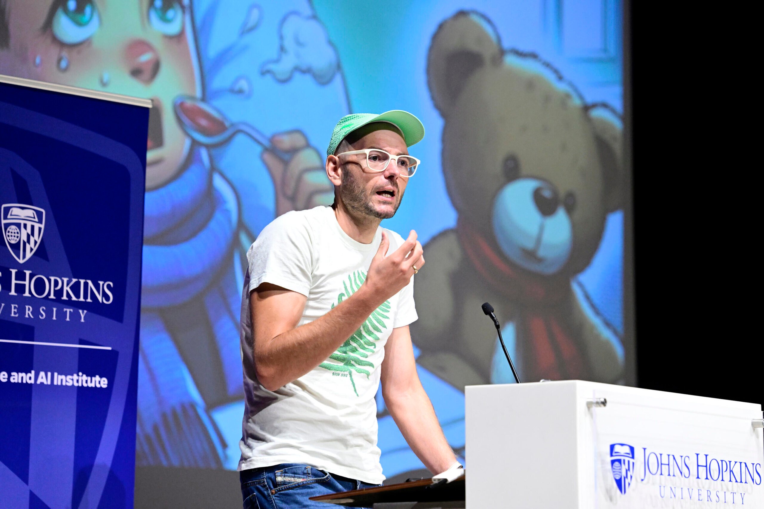 Mathias Unberath speaks on stage behind a podium in front of a screen displaying an illustration of a sick child holding a teddy bear.