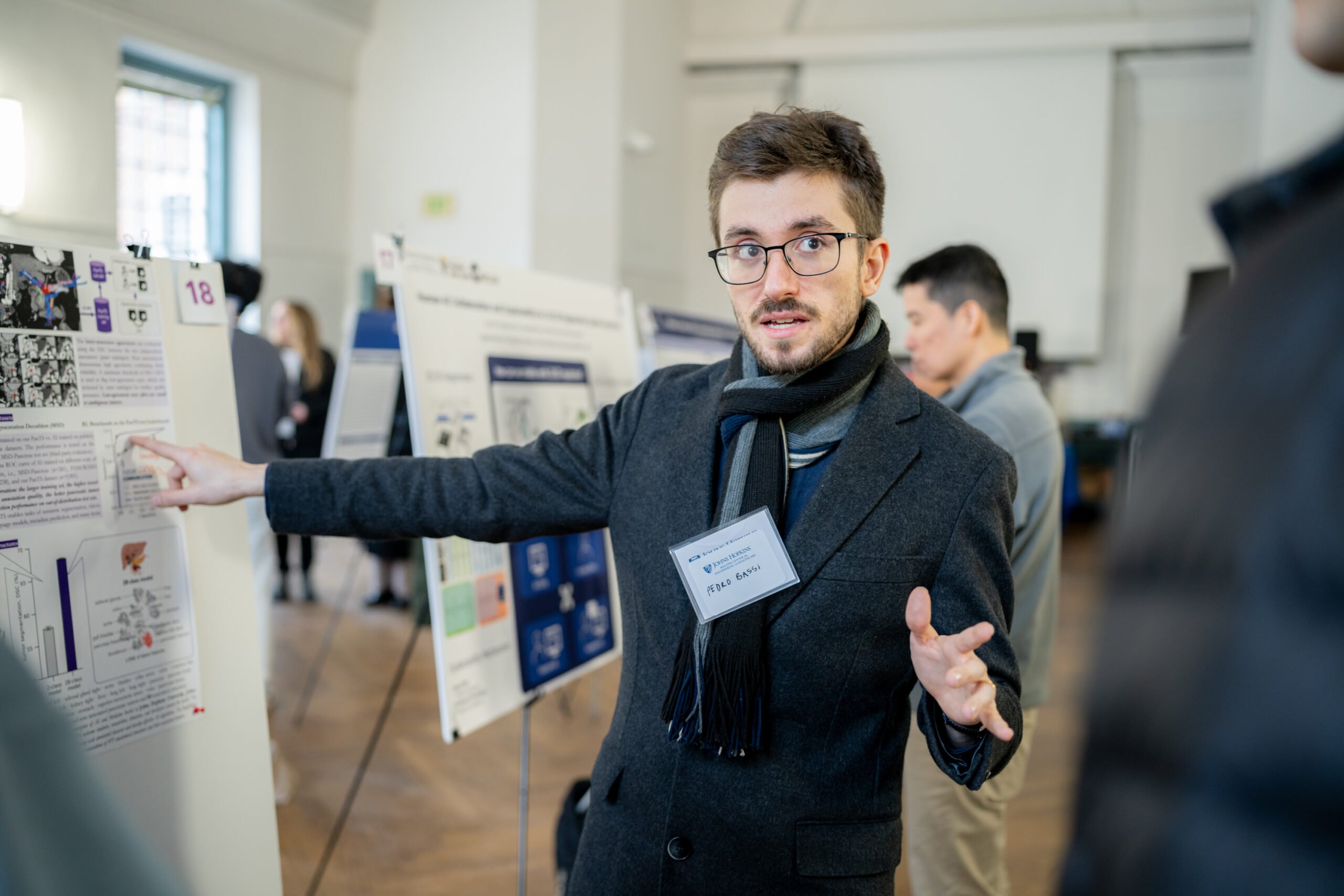 Malone_Symposium_25-51 Pedro R.A.S. Bassi presents a poster to an onlooker.