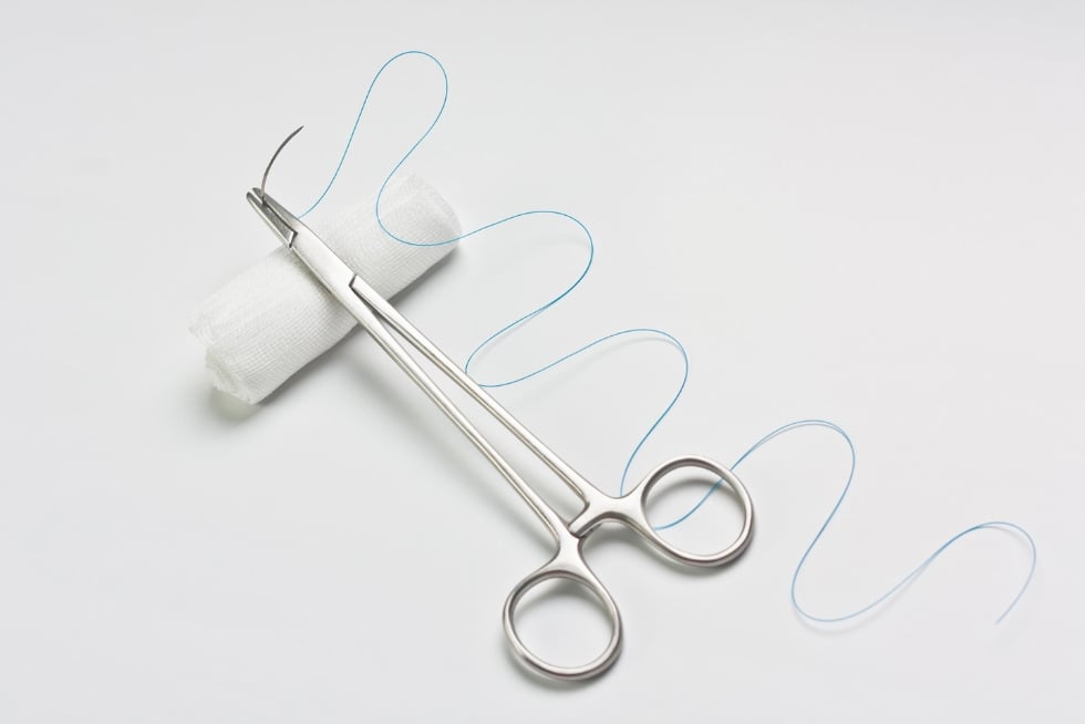 Needle holder put on white bandage as suture set.